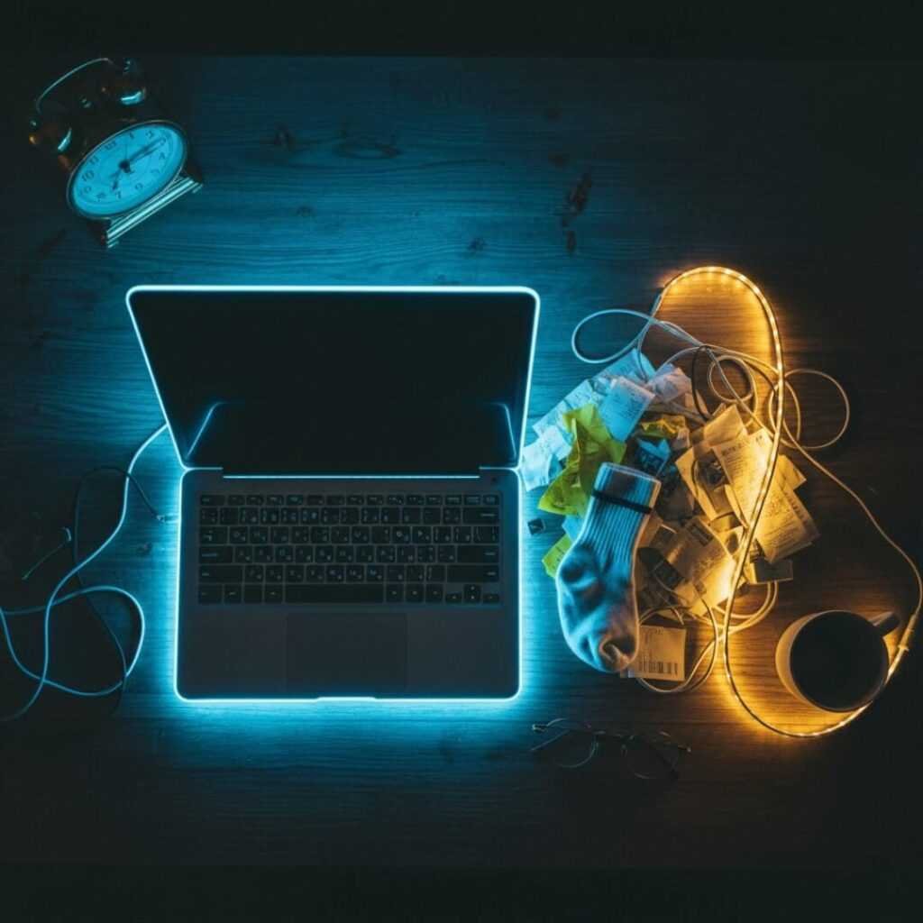 Top-down view of messy desk with LED-outlined laptop and random items.